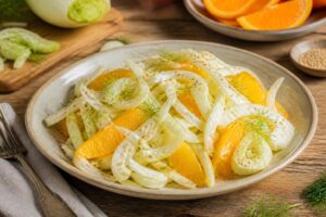 Salade de fenouil cru émincé à l'orange et au sésame grillé, servie dans un bol blanc avec une vinaigrette dorée et des herbes fraîches