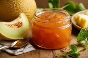 Pot de confiture de melon d'Espagne maison ouvert sur une table en bois, avec des tranches de melon à chair orangée et un couteau à confiture à côté