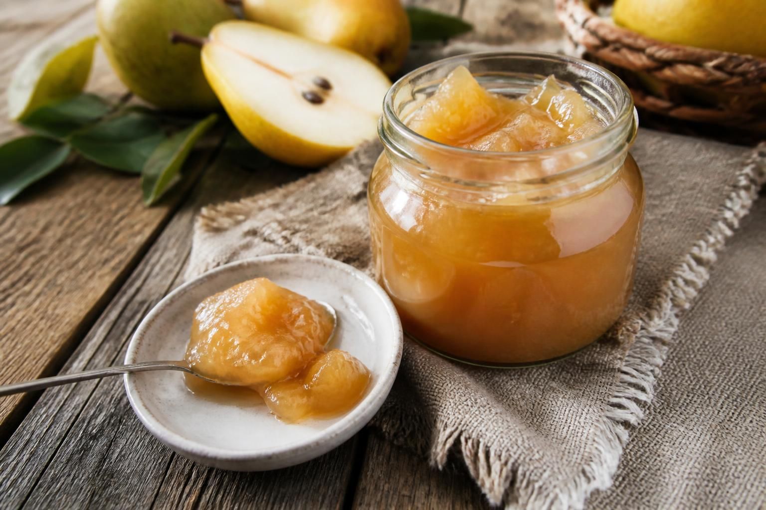Pot de confiture de poires maison au Confisuc, avec des poires fraîches et une cuillère en bois sur une table en bois rustique