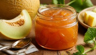 Pot de confiture de melon d'Espagne maison ouvert sur une table en bois, avec des tranches de melon à chair orangée et un couteau à confiture à côté