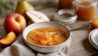 Pot de confiture pêche poire maison ouvert, avec des pêches jaunes et des poires fraîches posées à côté sur un torchon en lin