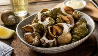 Bulots vivants cuits au court-bouillon servis dans un bol blanc avec une mayonnaise maison, vue de dessus sur fond de bois clair