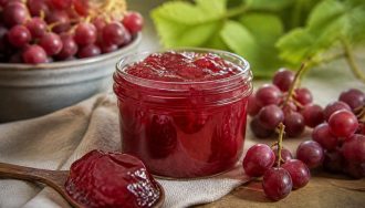 Pot de gelée de raisins rouges maison, couleur rubis translucide, posé sur une planche en bois avec des grappes de raisins rouges frais autour