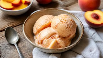 Glace pêche-yaourt maison sans sorbetière, servie dans une coupe transparente avec des tranches de pêche fraîche et des feuilles de menthe