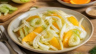 Salade de fenouil cru émincé à l'orange et au sésame grillé, servie dans un bol blanc avec une vinaigrette dorée et des herbes fraîches